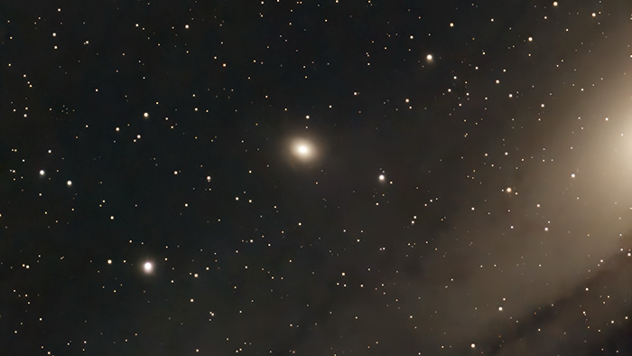 The Messier 32 galaxy shows as a central lighted smudge hovering above an arm of the Andromeda Galaxy.