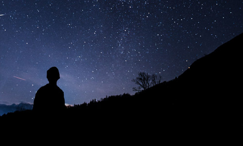 Young man at dusk looking up at the stars.