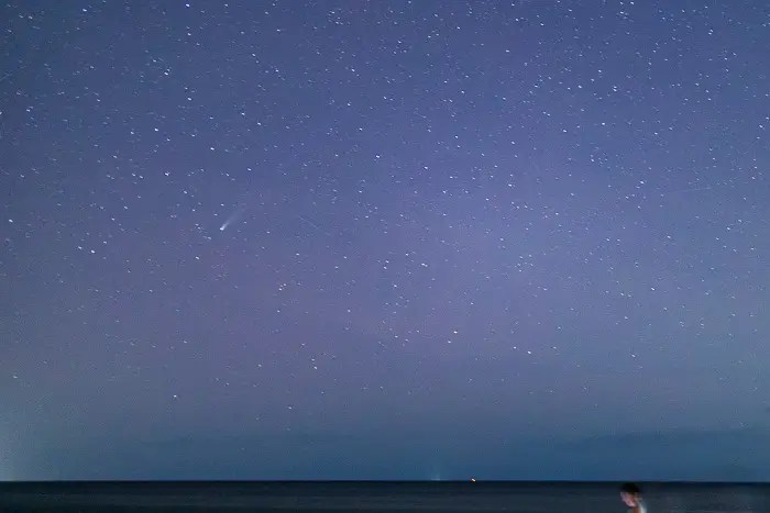 Shows Comet Lemmon with tail over Captiva Island with Gulf below and blue dark sky.