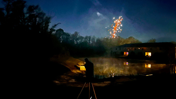 A Seestar S50 telescope in the foreground with stars above and fireworks from New Year party 