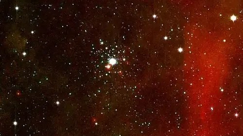 Shows open star cluster NGC 2362 with faint nebulosity in red beside it. NASA photo.