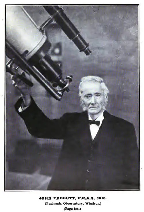 Black and white photo of John Tebbutt by his telescope in 1915.